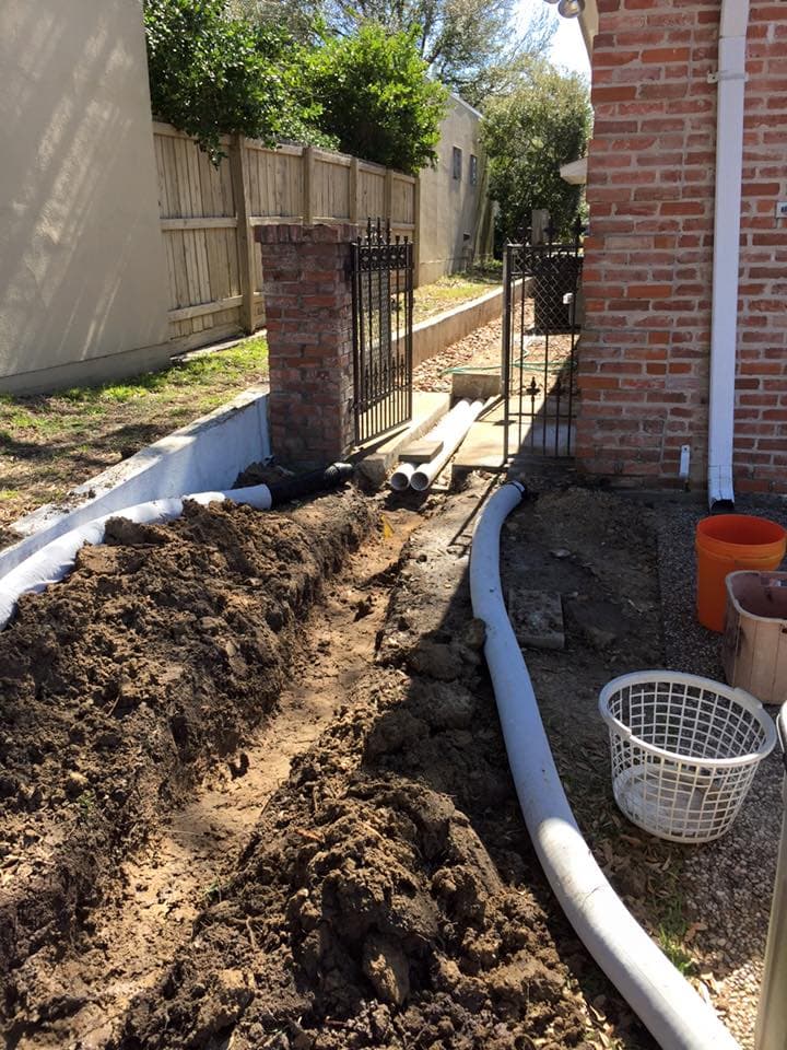 French drain trench with new PVC pipe installed along a brick gated entry walkway in Huntsville, TX