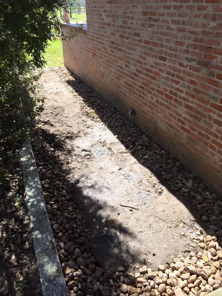 River rock drainage channel with catch basin installed along a brick building foundation in Huntsville, TX