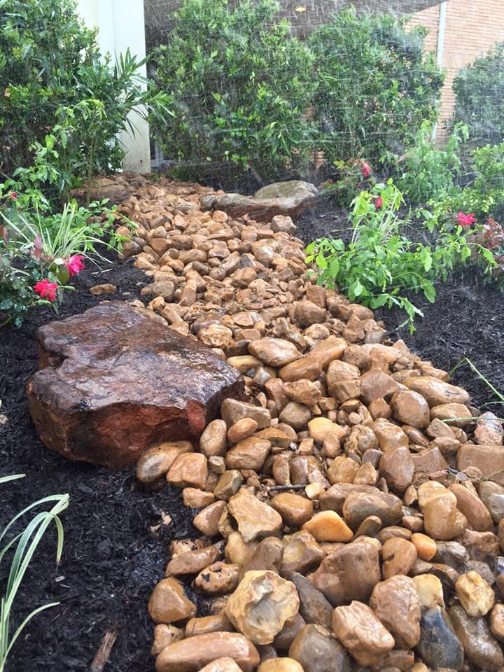 River rock drainage channel directing runoff through a planted garden bed during rainfall