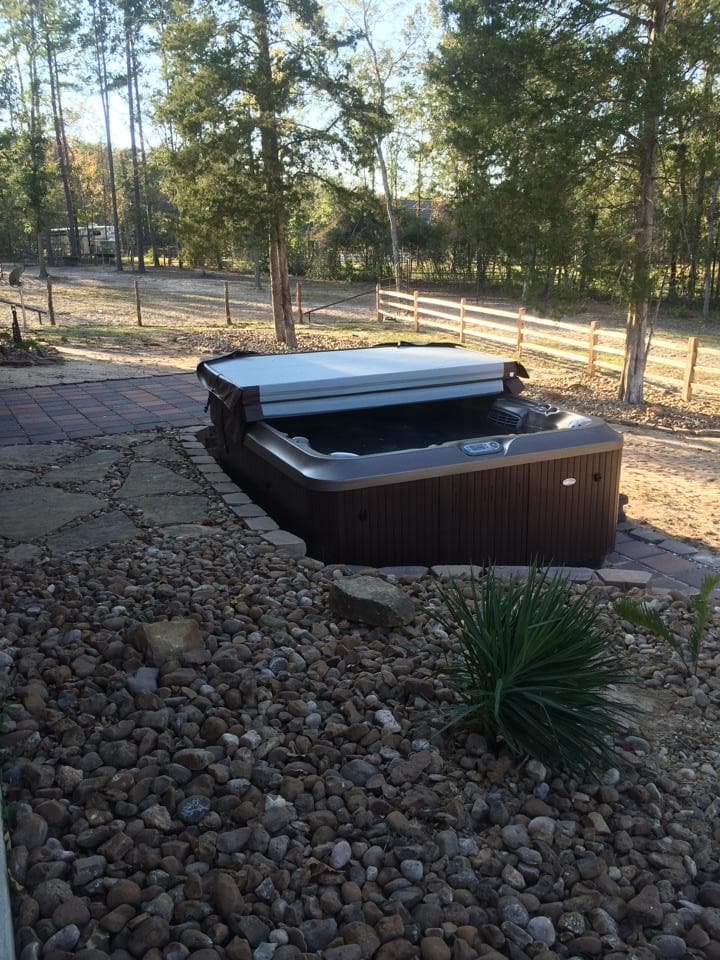 In-ground hot tub set into a brick paver patio surrounded by river rock in Huntsville, TX