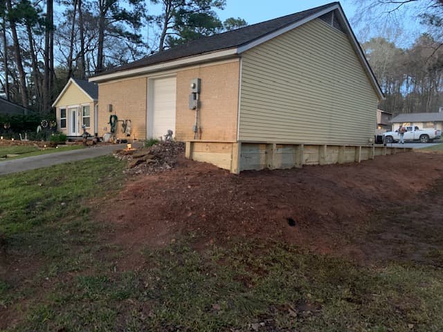 Wood retaining wall under construction beside a brick garage on a Huntsville, TX property