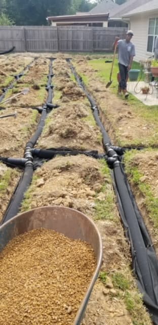 Drainage trenches with irrigation pipe and gravel backfill being installed in a Huntsville, TX backyard