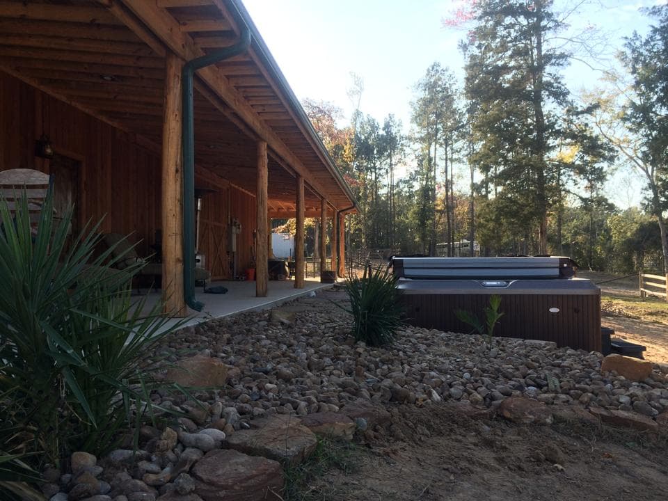 Hot tub installed beside a wood-post barn pavilion with a river rock surround on a Walker County ranch