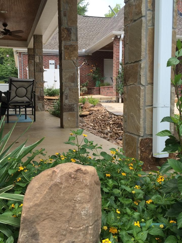 Rock-lined drainage path along a stone-column porch directing water away from a Huntsville, TX home