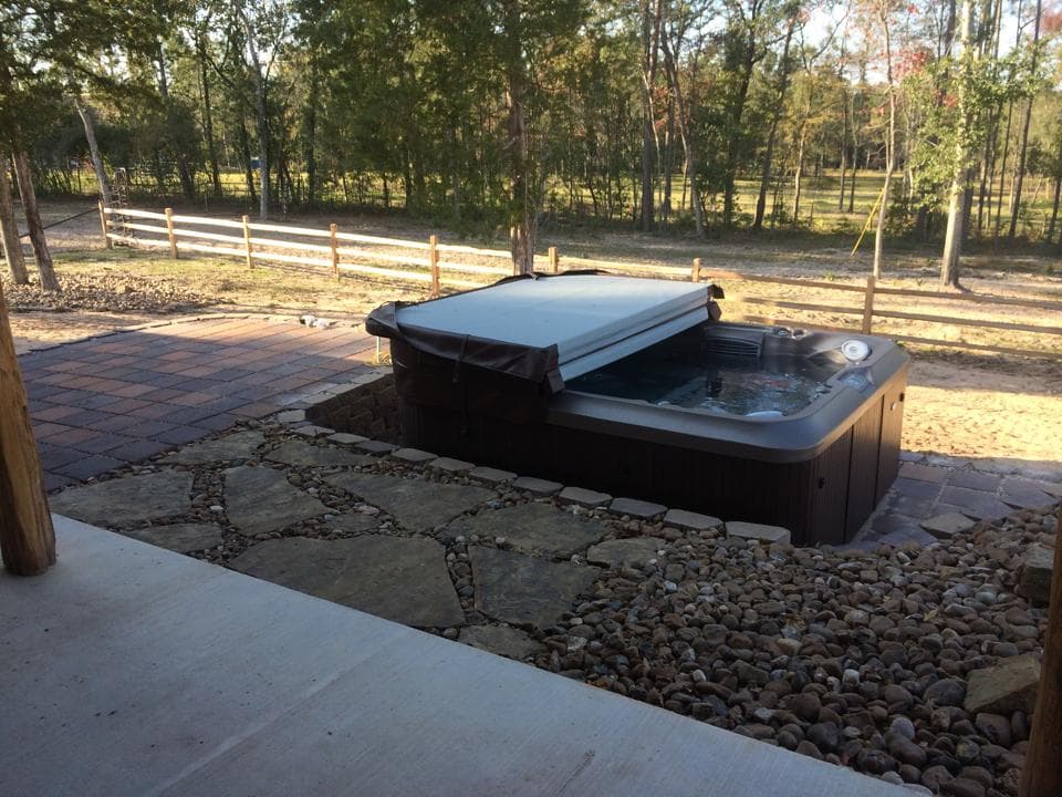 Hot tub set into a flagstone patio with a wood-post pergola frame and pasture view in Walker County, TX