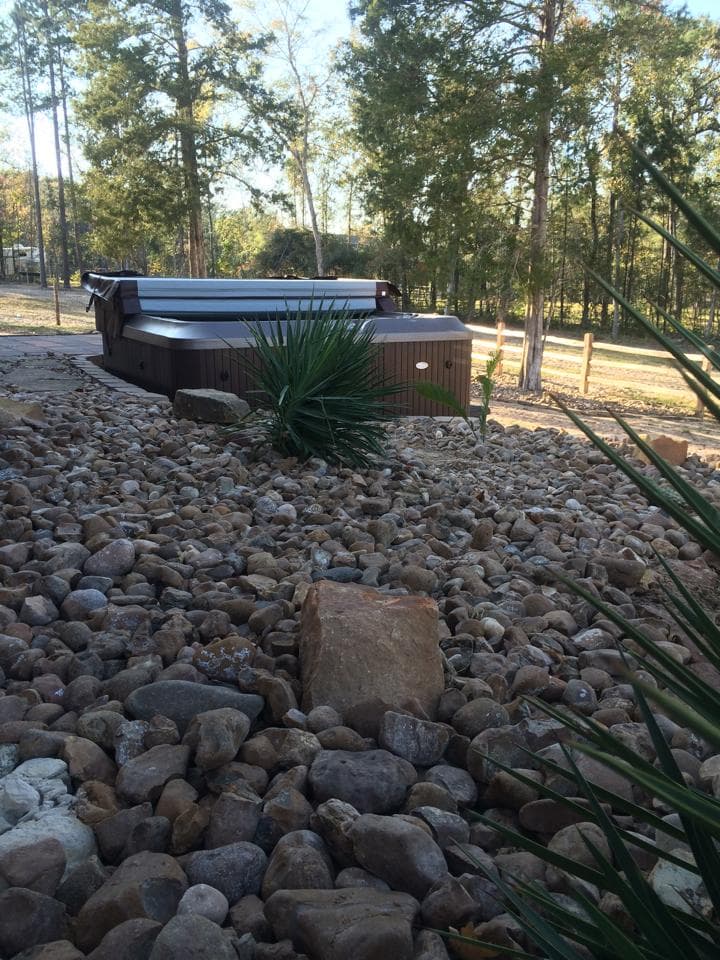 River rock hardscape surround built around a backyard hot tub installation near Huntsville, TX