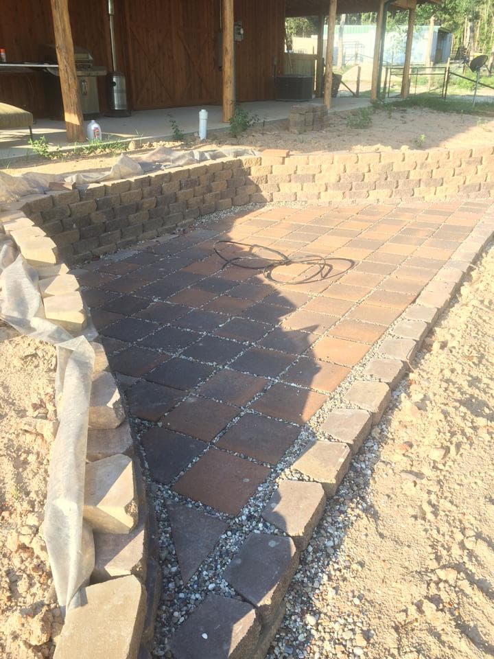 Segmental block retaining wall bordering a diamond-pattern paver patio under construction