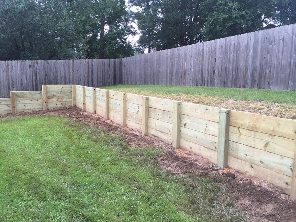 Long curved wood retaining wall built by Rockin' D Services along a backyard fence line in Huntsville, TX