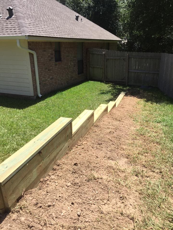 Wood retaining wall installed beside a brick home with matching wood gate in Walker County, TX