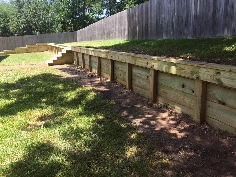 Stepped wood retaining wall installation showing tiered post and board construction