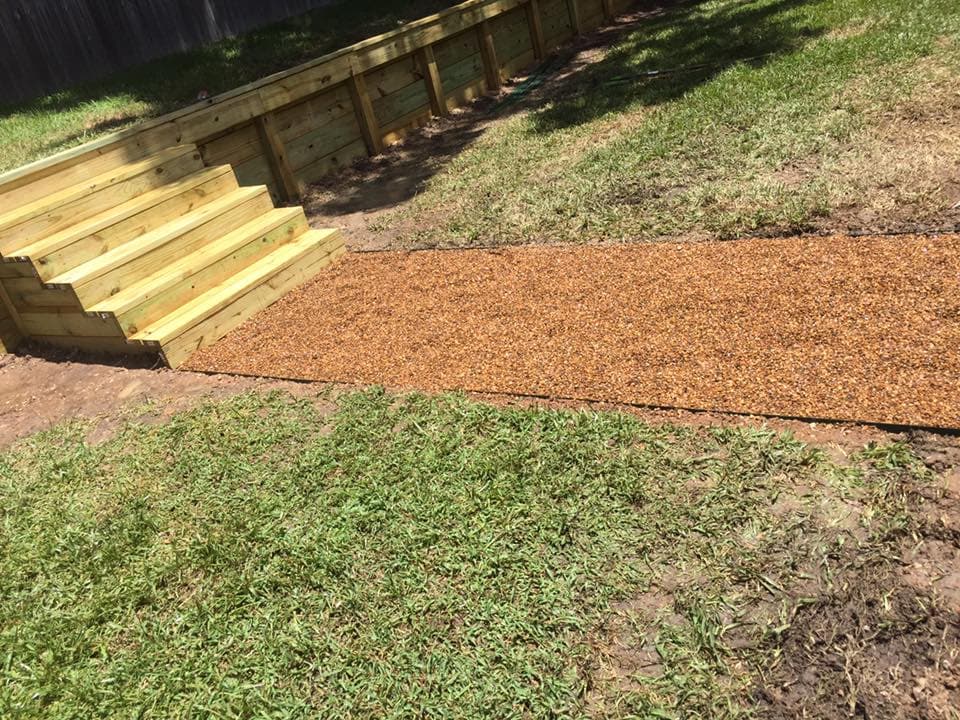 Wood retaining wall with built-in wood steps and gravel walkway landing in Huntsville, TX