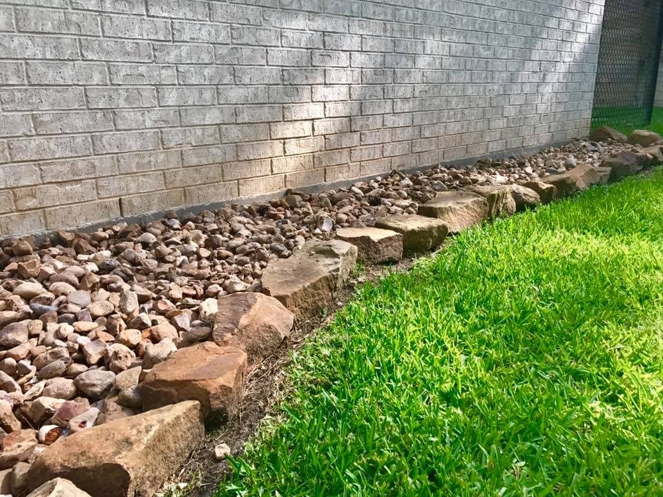 Rock drainage border installed along a home's brick foundation to direct water away in Huntsville, TX