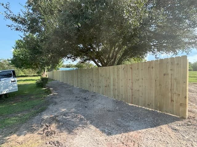 Wood privacy fence installed along a driveway beneath mature oak trees in Huntsville, TX