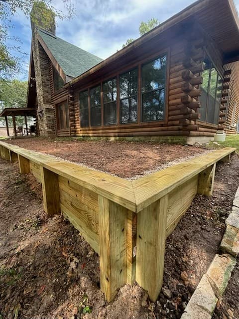 Close-up of a wood retaining wall corner post and board construction in front of a log cabin home in Huntsville, TX