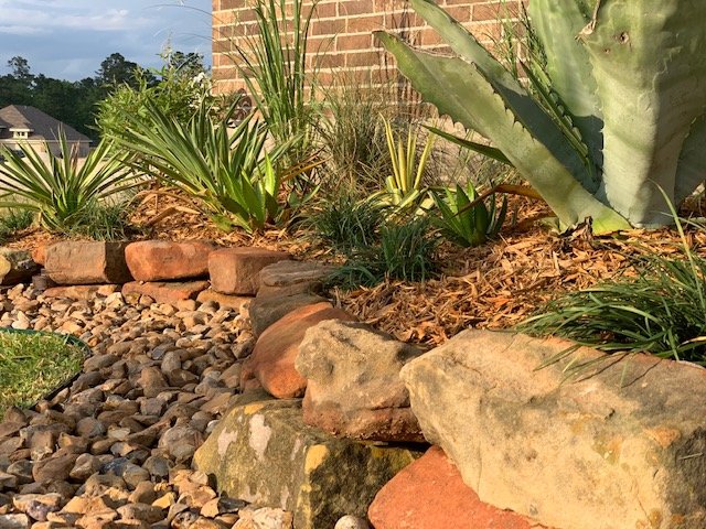 Finished landscape bed with plants and decorative stone by Rockin' D Services in Huntsville TX