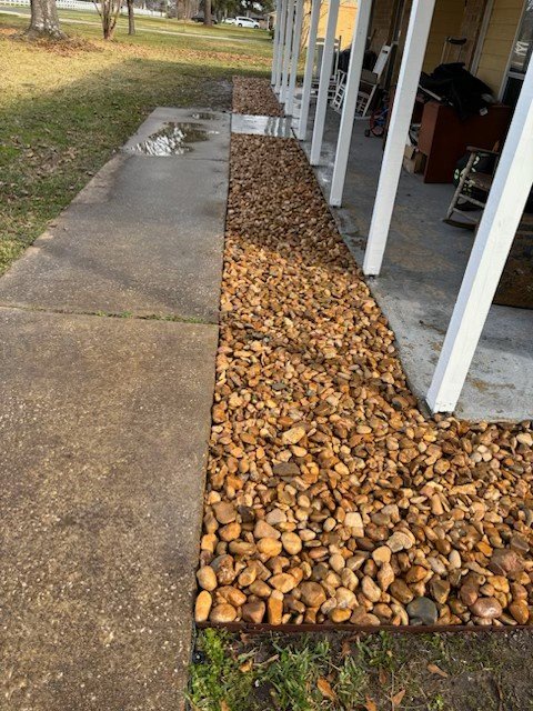 Completed french drain to appear as a decorative river rock drainage bed beside a patio installed by Rockin' D Services in Huntsville TX